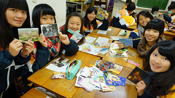 Asian students sitting around a table holding postcards