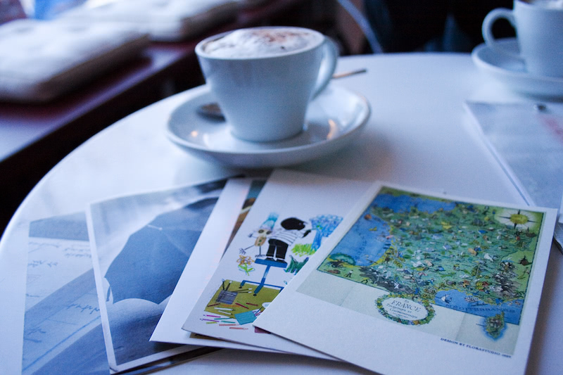 Assorted postcards on a cafe table, next to a cappuccino