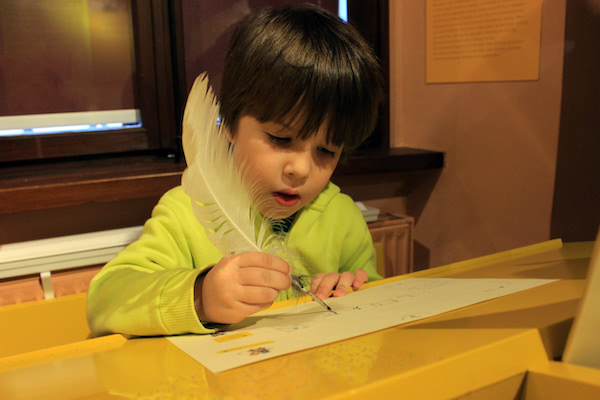 A child writes a letter with a quill at the Slovene Museum of Post and Telecommunications
