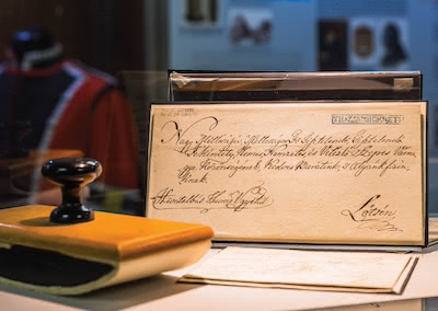 Handwritten historical letter in cursive, sealed with wax, displayed in a museum exhibit.